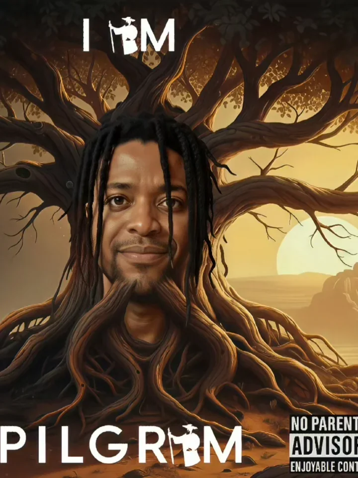 A man with dreadlocks framed by tree branches and roots.